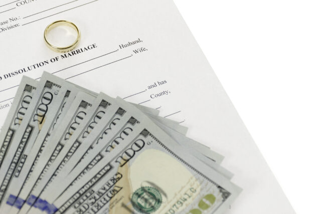 A stack of hundred-dollar bills and a wedding ring are placed on top of a legal document labeled 