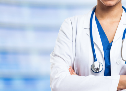 A healthcare professional in a white coat with a stethoscope draped around the neck, arms crossed. The background is blurred, creating a focus on the individual, who is likely a doctor or nurse. Only the torso and part of the face are visible.