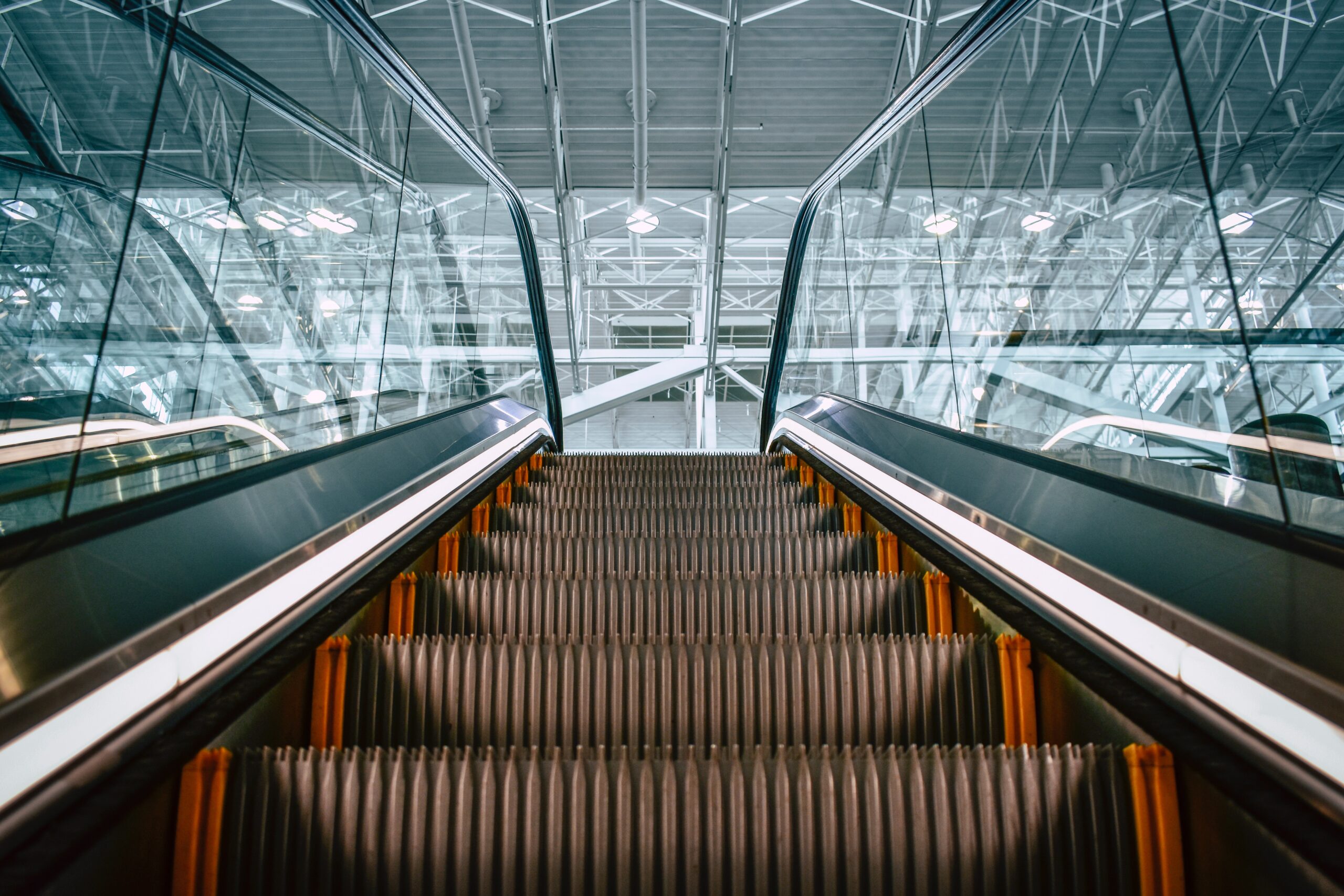 An empty escalator ascends in a modern, spacious building with a high ceiling and prominent structural beams. The sides of the escalator are glass with metal railings, and the environment appears clean and well-lit—a serene contrast to the recent Pennsylvania Escalator Accident still fresh in memory.