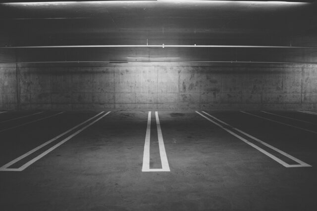 A dimly lit, empty parking garage with several marked parking spaces. The concrete walls and floor create an industrial feel. The lighting casts shadows, contributing to a somewhat eerie and desolate atmosphere. Be cautious as a slip and fall accident here could leave you injured in Pennsylvania, leaving you unsure of what to do next.