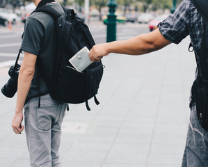 man taking wallet out of other man's backpack